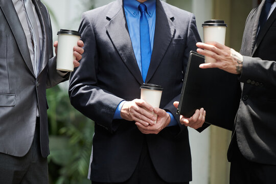 Cropped image of business people in formal suits drinking take out coffee and discussing work