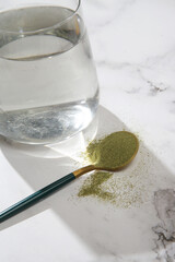 Green powder in spoon and glass of water. Concept of nutritional supplement, dieting, detox,...