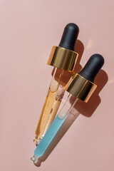 close up of two pipettes with pouring liquid serum and shadows on beige background. Trendy...