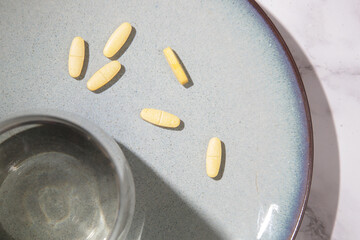 Glass of water and yellow pills, collagen, vitamins, omega 3, biotin or iron. Dietary supplements, preventive healthcare concept.