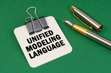 On a green surface, a pen and a sheet of paper with the inscription - Unified Modeling Language