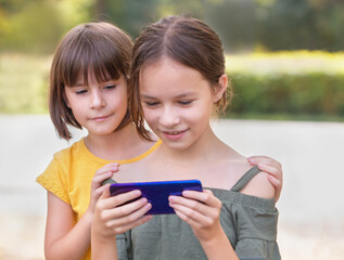 Twee gelukkige meisjes kijken naar mobiele telefoon. Mooie kinderen die internetten in het park