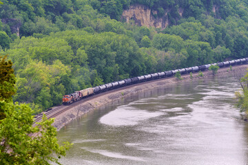 Diesel powered train engine pulling a string of tank cars along the Mississippi river.