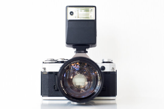 Classic 35mm film camera with telephoto lens and flash, on isolated white background