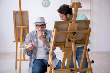 Old painter teaching young student at studio