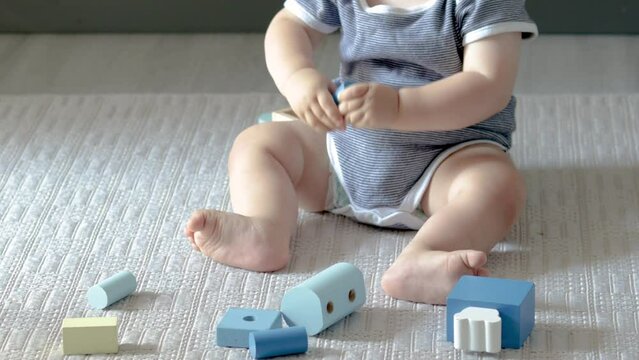 cute baby boy playing with eco wooden toys,train with carriages with cylinders and square form shapes.toddler on the floor,carpet,in kitchen is putting in mouth wood toys.adorable infant,maternity