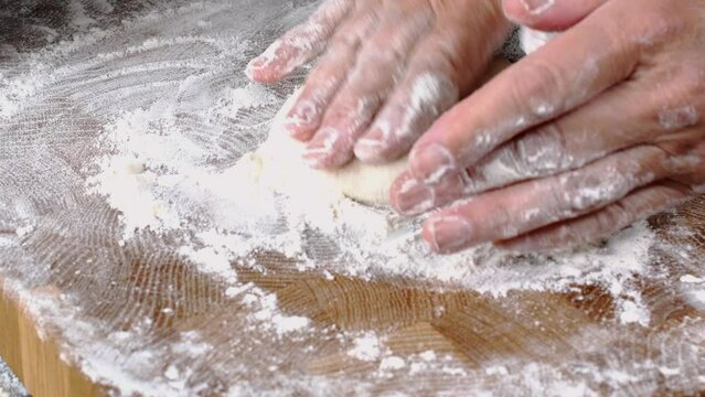 Human hands roll out fresh dough for make bread or pizza on kitchen board for baking.