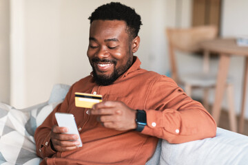 African Guy Shopping Online Using Cellphone And Credit Card Indoors