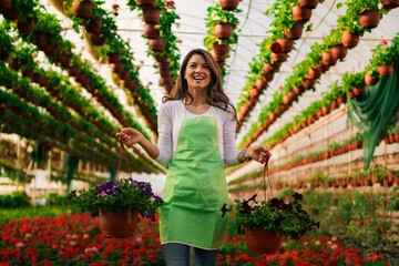 Happy nursery garden worker holding pots with flowers and relocating it.