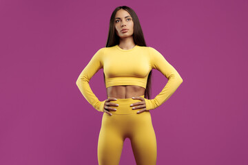Obraz na płótnie Canvas Confident amazing fit young brunette woman posing over purple background. Power and motivation concept.