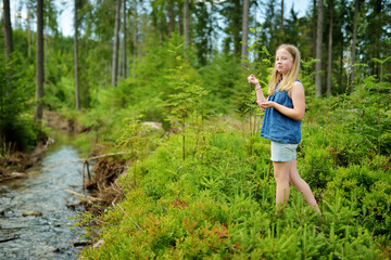 Young girl near cold shallow stream winding through majestic pine trees of Tatra mountain range near Zakopane, Poland.