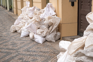 Fototapeta na wymiar Big white reusable recycling package, filled bags on the city street, piled up in a big pile on a paving stones.