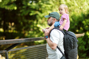 Young father and his toddler son watching animals at the zoo on warm and sunny summer day. Child...