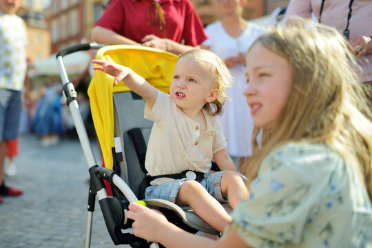 Cute toddler boy and his older sister explore beautiful streets of Warsaw's Old Town. Teenage girl and her brother in a stroller outdoors.