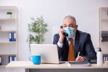 Old male employee working in the office during pandemic