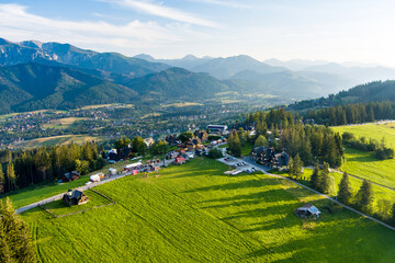 Fototapeta na wymiar Aerial view of Zakopane town underneath Tatra Mountains taken from the Gubalowka mountain range. High mountains and green hills in summer or spring.