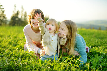 Two sisters and their toddler brother having fun outdoors on sunny summer day. Children exploring...