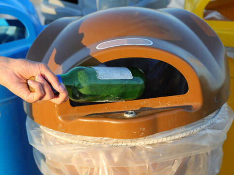 Hand Of Person Throwing Away A Glass Bottle In The Recycling Bin