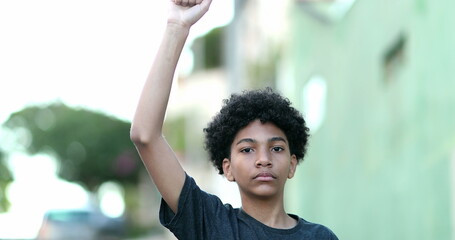 Young black boy raising fist in the air, kid looking at camera in protest