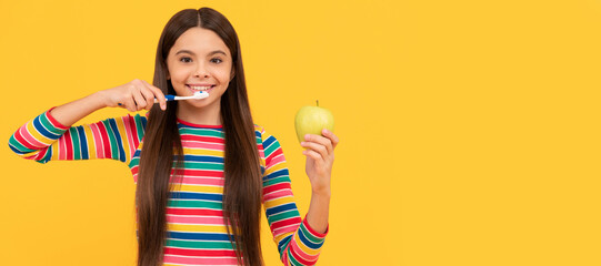 Happy girl child brush teeth with toothbrush holding apple yellow background, healthy teeth. Banner of child girl with teeth brush, studio portrait, header with copy space.