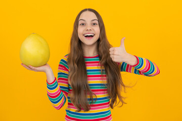 Teenager child girl hold citrus fruit pummelo or pomelo full of vitamin, isolated on yellow...