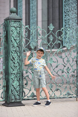Fashion kid. Cute russian boy, fun child in Moscow city, Russia. Summer stylish look for child, fashionable kid. Street style. DPAM clothes. Architectural fashion. Outfit for child, kid. Shorts, cap