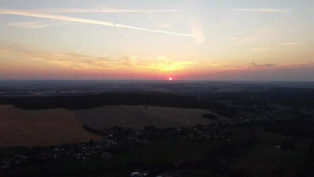 Drohnenmaterial beim Sonnenuntergang &uuml;ber einem Dorf und kleinen Wald