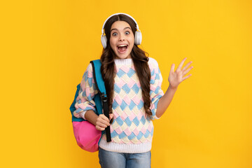 Excited face. School girl, teenager student in headphones on yellow isolated studio background. Music school concept. Amazed expression, cheerful and glad.