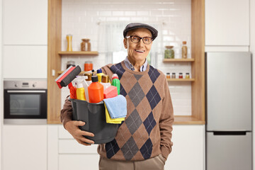 Elderly man holding a bucket with cleaning supplies and standing in a kitchen