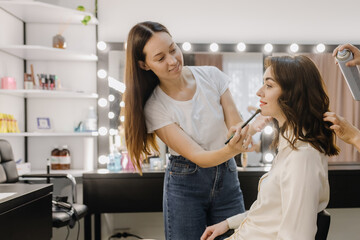 Girls do makeup and hair in the showroom. Two beautiful girls are having fun and smiling. They are in a bright room near a mirror.
