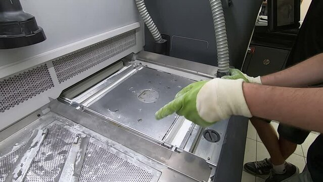 A male worker cleans the surface of an industrial 3D printer from white powder with a vacuum cleaner close-up. Multi Jet Fusion MJF 3D printing. The working process