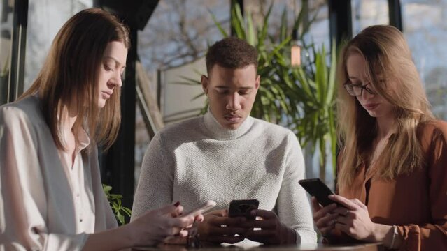 Three friends in a cafe bar using phone. Looking at smartphones unconscious about the surroundings..
