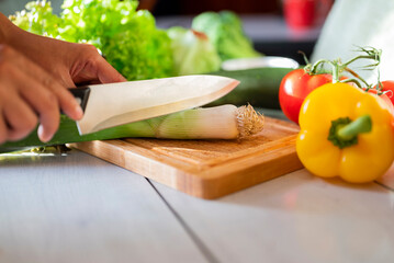 girl cook in the kitchen cuts celery with vegetables on a wooden board with a knife