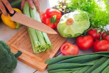 girl cook in the kitchen cuts celery with vegetables on a wooden board with a knife