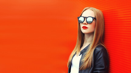 Portrait of stylish blonde young woman posing wearing sunglasses in the city on red background