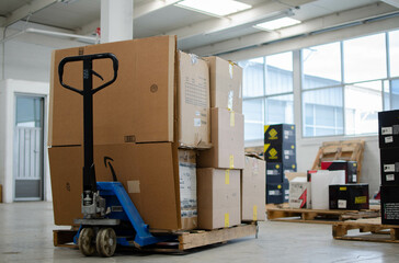 un patín hidráulico de carga moviendo una tarima con cajas de cartón, almacén