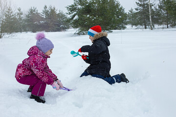 Fototapeta na wymiar A boy and a girl are outdoors in winter park, making snowballs with plastic sculpting tools.