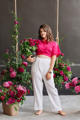 a brunette woman in white pants and a pink blouse with peonies and a swing.