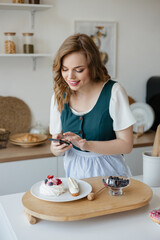 Beautiful girl confectioner takes a photo of a cake in the kitchen