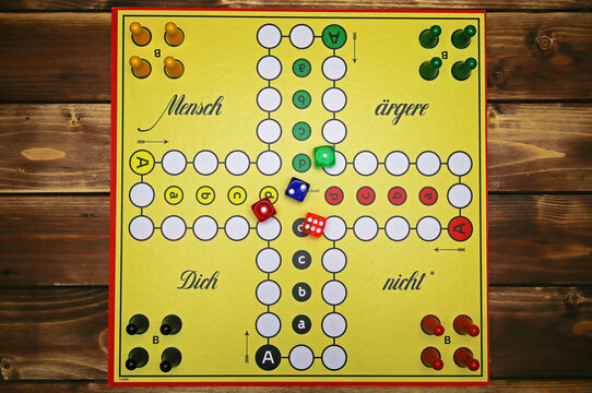 Viersen, Germany - May 9. 2021: Top down view on yellow strategy game board with colorful pieces and dices of mensch &auml;rgere dich nicht, wooden background