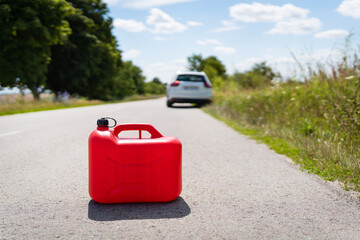 A car parked on the side of the road, an empty red canister. The driver is on the road. Help on the road. Fuel shortage - oil, diesel, gasoline.