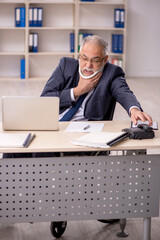 Old male employee after accident sitting at workplace
