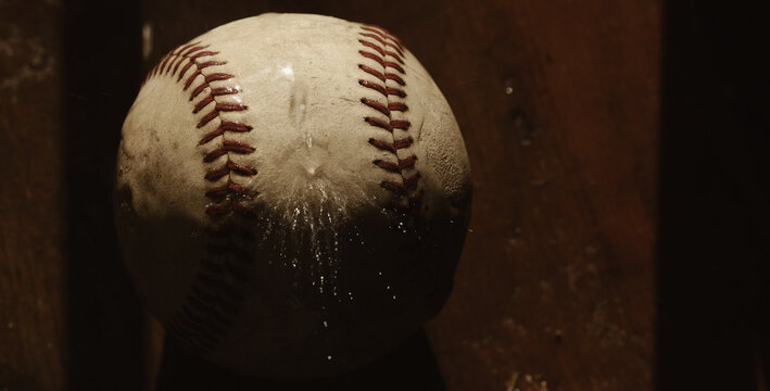 Old used baseball ball closeup with worn texture under water, rain game concept.