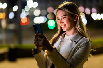 Beautiful young woman texting on the phone in the city at night.