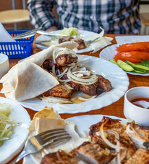 fried sliced kebab on a plate with onions cucumbers pita bread and sauce. wooden table.