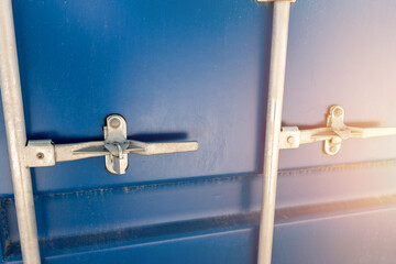 Close-up detail view of big blue metal freight cargo container door handle closed with padlock...