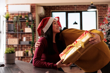 Young person receiving christmas present from coworker to celebrate xmas holiday in office with festive decorations and seasonal winter ornaments. Giving gifts to colleagues in business space.