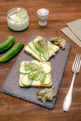 Bruschetta sandwich bread toast with soft green avocado cheese ricotta,fresh cucumbers,basil greenery on wooden cutting board.Tasty healthy vegetarian food,Italian cuisine appetizer.top view flat lay