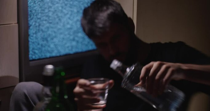 Drunk white male in his 30s-40s sits on the floor in apartment next to white noise TV. Hard drinking,  lot of empty bottles on the floor. Concept of depression, alcohol addiction and utility bills.