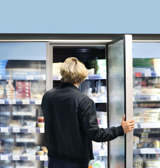 Fototapeta na wymiar Man choosing frozen food from a supermarket freezer., reading product information